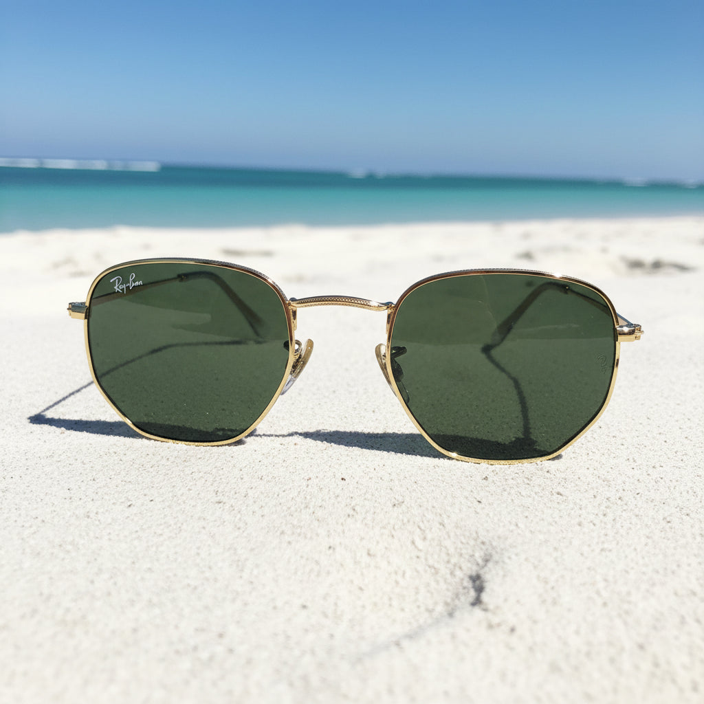 Ray-Ban aviator-style sunglasses with gold metal frames and dark green lenses, displayed with a light gray microfiber cleaning cloth, black case, and Ray-Ban box on a white surface.